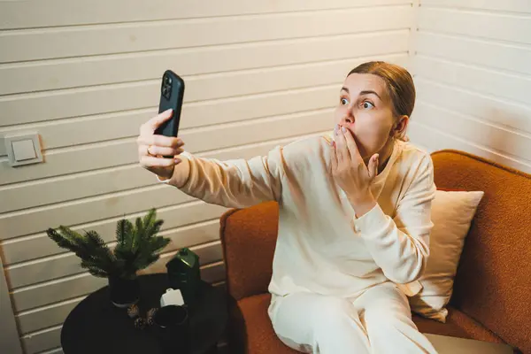 Stock image A woman in home clothes is sitting at home on the sofa with a laptop and talking on the phone. Work from home.