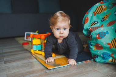 Mavi gözlü bir bebek yerde yatar ve kameraya bakar. Gri şortlu, beyaz saçlı bir bebek evde oynuyor. Bebekler için kıyafetler..