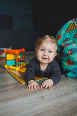 Mavi gözlü bir bebek yerde yatar ve kameraya bakar. Gri şortlu, beyaz saçlı bir bebek evde oynuyor. Bebekler için kıyafetler..