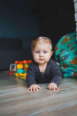 Mavi gözlü bir bebek yerde yatar ve kameraya bakar. Gri şortlu, beyaz saçlı bir bebek evde oynuyor. Bebekler için kıyafetler..