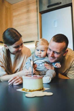 Küçük bir oğlu olan genç bir çift mutfakta pastayla. Aileler oğullarının doğum gününü kutlarlar..