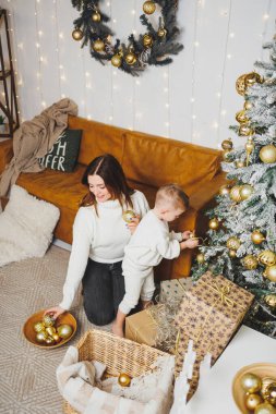 Anne ve oğlu Noel ağacını yeni yıl için süsler. Aile çevresindeki Noel ağacı. Oda yeni yıl için dekore edildi.