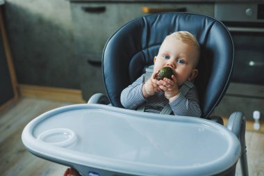 Bir erkek bebek lezzetli bir avokado yer. Bebeğin ilk yemeği. Çocuk bir avokado yiyor.
