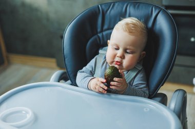Bir erkek bebek lezzetli bir avokado yer. Bebeğin ilk yemeği. Çocuk bir avokado yiyor.
