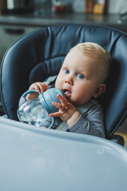 Bebek plastik bir bardaktan pipetle su içiyor. Bebekler için sofra takımı.