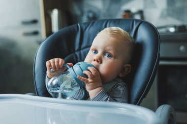Bebek plastik bir bardaktan pipetle su içiyor. Bebekler için sofra takımı.