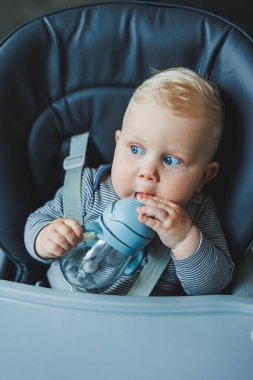 Bebek plastik bir bardaktan pipetle su içiyor. Bebekler için sofra takımı.