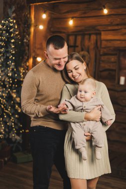 Mutlu bir aile çifti, kollarında bir çocukla bir Noel ağacının arkasında. Bebekli bir yeni yıl. Aile Yeni Yıl Ortamı.