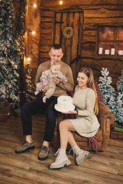 Küçük bir çocuklu mutlu bir genç aile, yeni yılı parlak bir evde, Noel ağacının yanında öpüşerek ve kucaklaşarak kutluyor. Aile çemberinde yeni yıl..