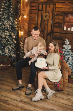 Küçük bir çocuklu mutlu bir genç aile, yeni yılı parlak bir evde, Noel ağacının yanında öpüşerek ve kucaklaşarak kutluyor. Aile çemberinde yeni yıl..