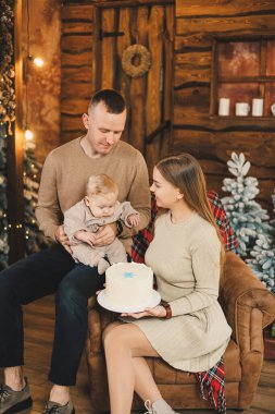 Küçük bir çocuklu mutlu bir genç aile, yeni yılı parlak bir evde, Noel ağacının yanında öpüşerek ve kucaklaşarak kutluyor. Aile çemberinde yeni yıl..