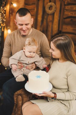 Küçük bir çocuklu mutlu bir genç aile, yeni yılı parlak bir evde, Noel ağacının yanında öpüşerek ve kucaklaşarak kutluyor. Aile çemberinde yeni yıl..