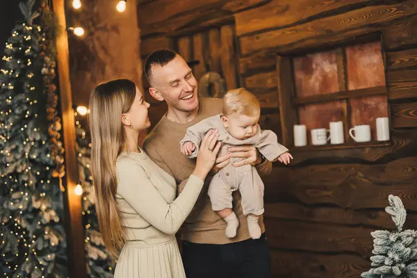 stock image The atmosphere of the Christmas holidays. A happy family with a small child celebrates the New Year together near the Christmas tree in a cozy house. Christmas in the family circle.