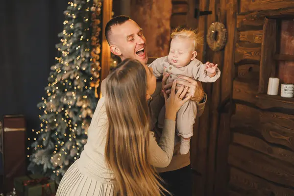 stock image The atmosphere of the Christmas holidays. A happy family with a small child celebrates the New Year together near the Christmas tree in a cozy house. Christmas in the family circle.