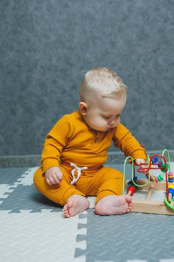 Vücut kıyafetli bir bebek yerde oturup eğitici oyuncaklarla oynar. Bir çocuğun iyi motor becerilerini geliştirmek için oyuncaklar.