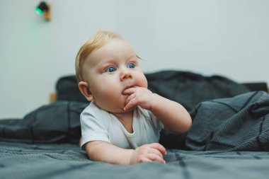 Beyaz elbiseli mavi gözlü bir bebek yüzünde bir gülümsemeyle bir yatakta yatıyor. Bebek karnının üstünde yatıyor. Bebeğin hisleri..