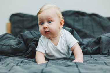 Beyaz elbiseli mavi gözlü bir bebek yüzünde bir gülümsemeyle bir yatakta yatıyor. Bebek karnının üstünde yatıyor. Bebeğin hisleri..