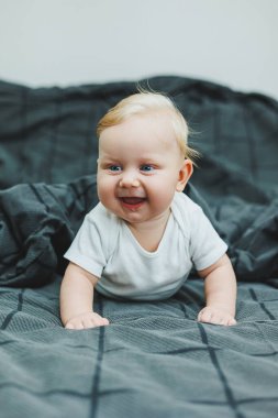 Beyaz elbiseli mavi gözlü bir bebek yüzünde bir gülümsemeyle bir yatakta yatıyor. Bebek karnının üstünde yatıyor. Bebeğin hisleri..