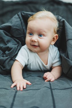 Beyaz elbiseli mavi gözlü bir bebek yüzünde bir gülümsemeyle bir yatakta yatıyor. Bebek karnının üstünde yatıyor. Bebeğin hisleri..