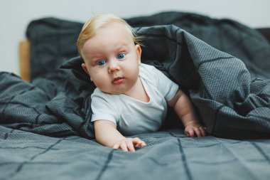 Beyaz elbiseli mavi gözlü bir bebek yüzünde bir gülümsemeyle bir yatakta yatıyor. Bebek karnının üstünde yatıyor. Bebeğin hisleri..