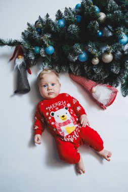 Mayo giymiş şirin bir bebek Noel ağacının ve hediye kutularının yanında yatıyor. Bebekler için yeni yıl kıyafetleri. kış yeni yıl konsepti.