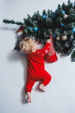 Mayo giymiş şirin bir bebek Noel ağacının ve hediye kutularının yanında yatıyor. Bebekler için yeni yıl kıyafetleri. kış yeni yıl konsepti.