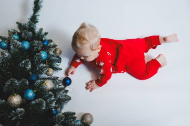 Mayo giymiş şirin bir bebek Noel ağacının ve hediye kutularının yanında yatıyor. Bebekler için yeni yıl kıyafetleri. kış yeni yıl konsepti.