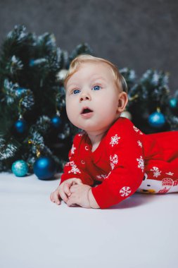 Mayo giymiş şirin bir bebek Noel ağacının ve hediye kutularının yanında yatıyor. Bebekler için yeni yıl kıyafetleri. kış yeni yıl konsepti.