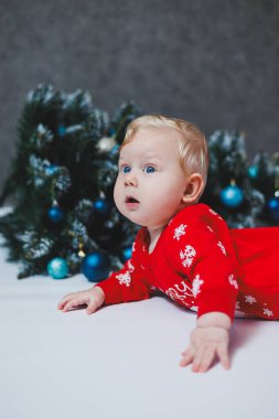 Mayo giymiş şirin bir bebek Noel ağacının ve hediye kutularının yanında yatıyor. Bebekler için yeni yıl kıyafetleri. kış yeni yıl konsepti.