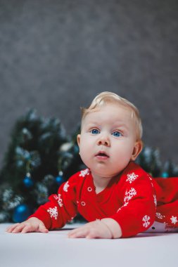 Mayo giymiş şirin bir bebek Noel ağacının ve hediye kutularının yanında yatıyor. Bebekler için yeni yıl kıyafetleri. kış yeni yıl konsepti.