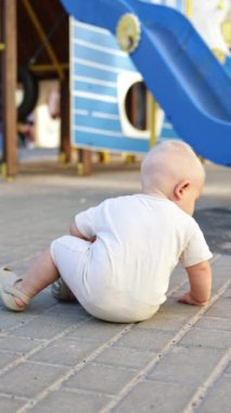 Bir yaşında bir çocuk yürüyüş sırasında asfalta tebeşirle resim çizer. Bir çocuk tebeşirle resim çizer. Bir çocuk için yaz giysileri..