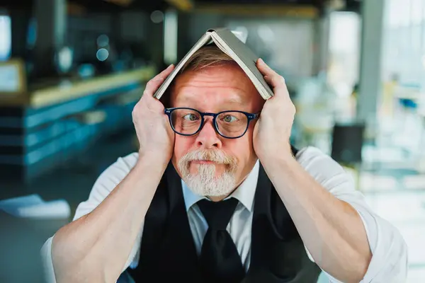 stock image Emotional old man in glasses with a notebook in the office. An old businessman grimaces on his forehead.