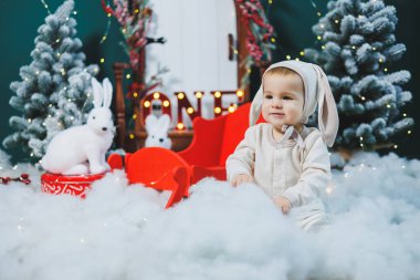 Tavşan kostümlü küçük bir çocuk Noel ağacının yanında oturuyor. Yeni yıl havası. Çocuklar için tavşan kostümü.