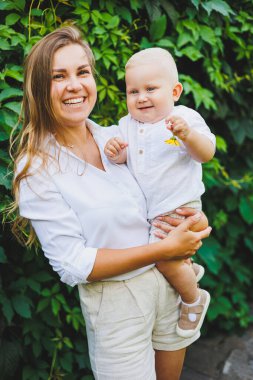 Genç ve mutlu bir anne yürüyüş sırasında bir yaşındaki oğlunu kollarına alır. Sevgi dolu bir anne oğluna sarılır..