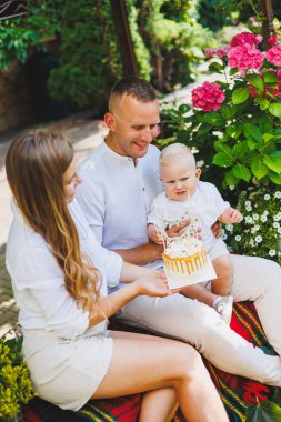 Anne ve baba doğada bir yaşındaki oğullarıyla birlikte ilk doğum gününü pastayla kutluyorlar. Doğumgünü Doğada bir pasta.