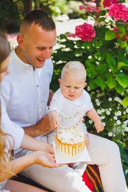 Anne ve baba doğada bir yaşındaki oğullarıyla birlikte ilk doğum gününü pastayla kutluyorlar. Doğumgünü Doğada bir pasta.