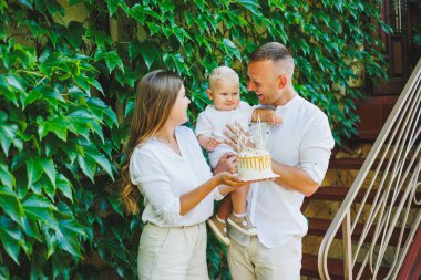 Anne ve baba doğada bir yaşındaki oğullarıyla birlikte ilk doğum gününü pastayla kutluyorlar. Doğumgünü Doğada bir pasta.