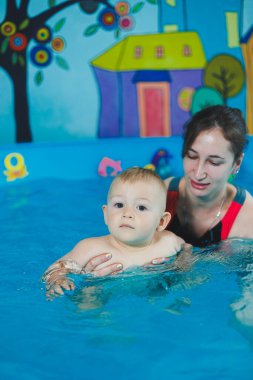 Bir antrenör küçük bir çocuğa çocuk havuzunda yüzmeyi öğretir. Bebeklere yüzmeyi öğretme kursları.