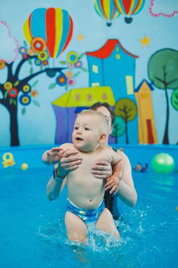Bir antrenör küçük bir çocuğa çocuk havuzunda yüzmeyi öğretir. Bebeklere yüzmeyi öğretme kursları.