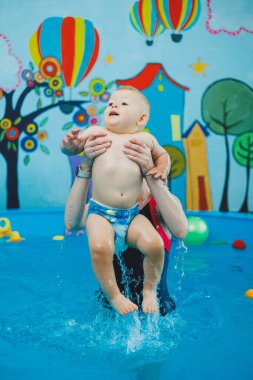 Bir antrenör küçük bir çocuğa çocuk havuzunda yüzmeyi öğretir. Bebeklere yüzmeyi öğretme kursları.
