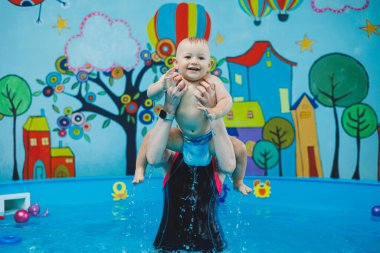 Bir antrenör küçük bir çocuğa çocuk havuzunda yüzmeyi öğretir. Bebeklere yüzmeyi öğretme kursları.