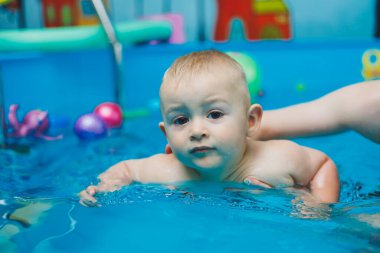 Bir antrenör küçük bir çocuğa çocuk havuzunda yüzmeyi öğretir. Bebeklere yüzmeyi öğretme kursları.