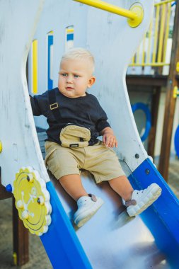 1 yaşında bir çocuk oyun parkındaki tepeden aşağı iniyor. Dışarıda bir bebek oynuyor. Çocuk gelişimi.