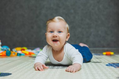 Altı aylık küçük bir çocuk karnının üstüne yatmayı öğreniyor. Bebek yerde oyuncaklarla oynuyor..
