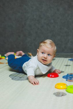 Altı aylık küçük bir çocuk karnının üstüne yatmayı öğreniyor. Bebek yerde oyuncaklarla oynuyor..