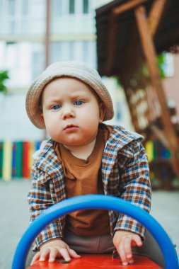 Bebek çocuk parkta salıncakta sallanıyor. Sokakta bir çocuk oynuyor.