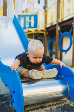 1 yaşında bir çocuk oyun parkındaki tepeden aşağı iniyor. Dışarıda bir bebek oynuyor. Çocuk gelişimi.
