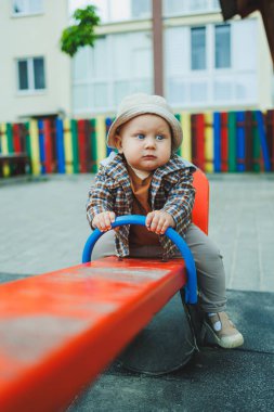 Bebek çocuk parkta salıncakta sallanıyor. Sokakta bir çocuk oynuyor.