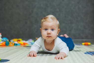 Altı aylık küçük bir çocuk karnının üstüne yatmayı öğreniyor. Bebek yerde oyuncaklarla oynuyor..