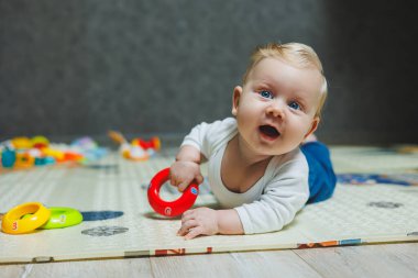 Altı aylık küçük bir çocuk karnının üstüne yatmayı öğreniyor. Bebek yerde oyuncaklarla oynuyor..